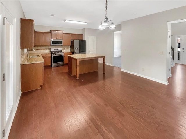 kitchen featuring stainless steel appliances, dark wood-type flooring, a sink, brown cabinetry, and decorative light fixtures