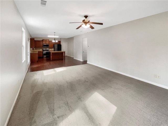 unfurnished living room with visible vents, a sink, baseboards, and ceiling fan with notable chandelier