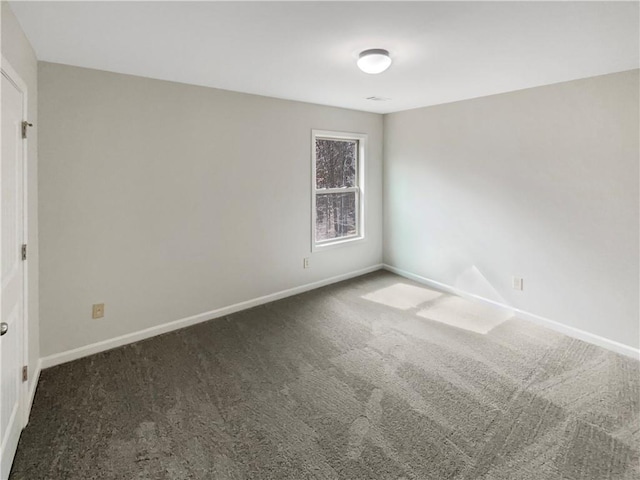 empty room featuring dark colored carpet and baseboards