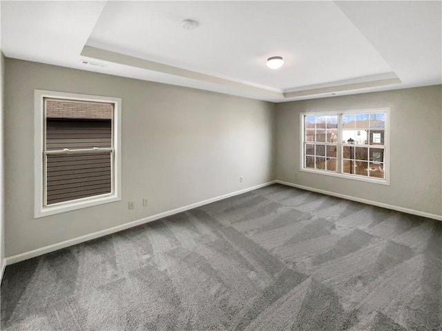 spare room with baseboards, visible vents, a tray ceiling, and dark colored carpet