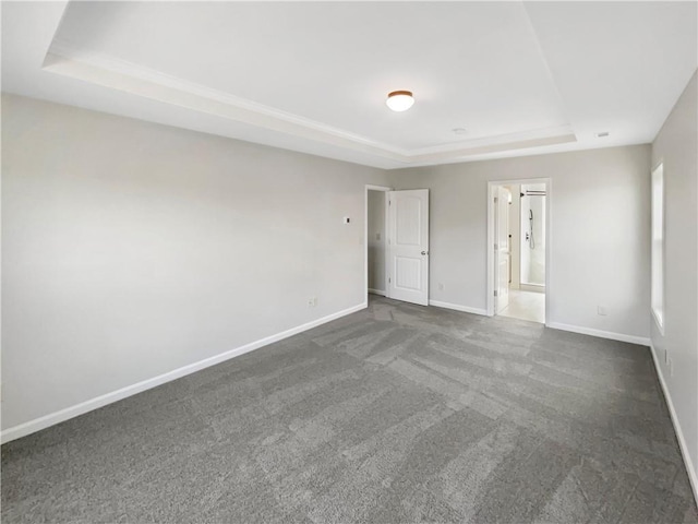 empty room featuring dark colored carpet, a raised ceiling, and baseboards