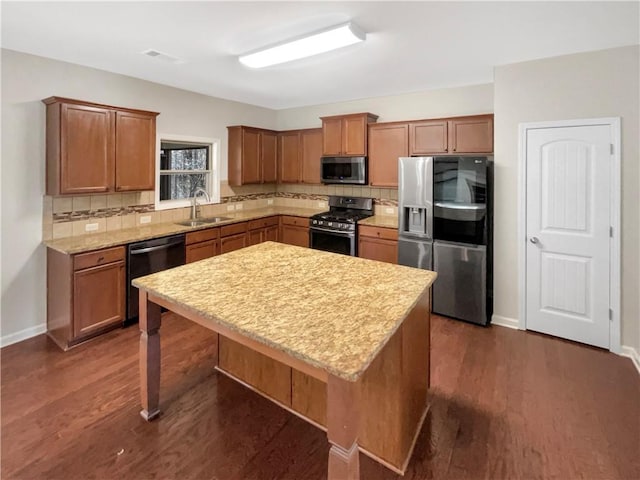 kitchen with a sink, appliances with stainless steel finishes, brown cabinetry, and a kitchen island