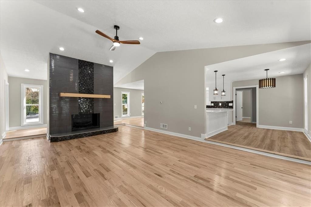 unfurnished living room with lofted ceiling, a fireplace, ceiling fan, and light wood-type flooring