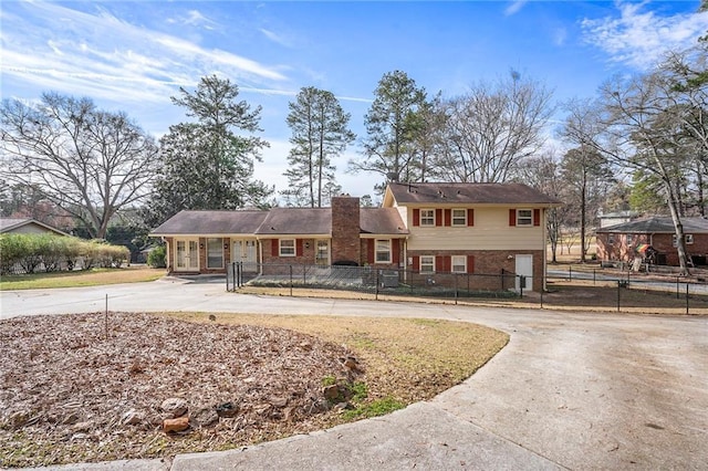 tri-level home with a fenced front yard, a chimney, concrete driveway, and brick siding