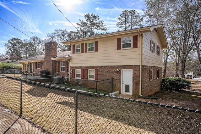 tri-level home with central AC, a chimney, brick siding, and a fenced backyard