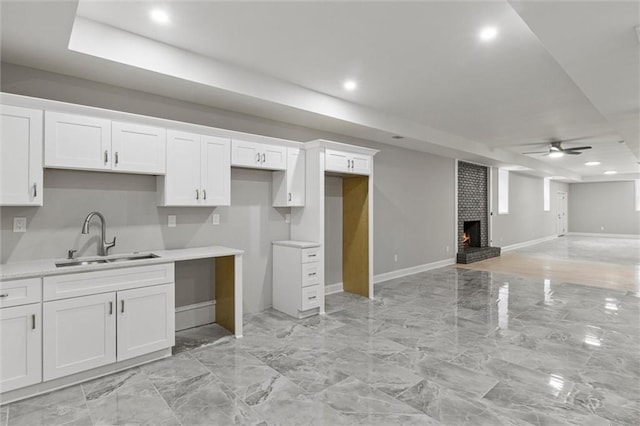 kitchen with white cabinets, a brick fireplace, ceiling fan, and sink