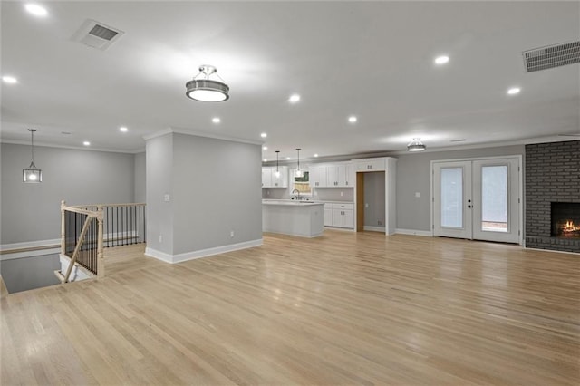 unfurnished living room with crown molding, a fireplace, sink, and light hardwood / wood-style flooring