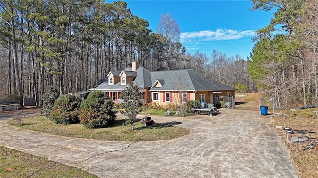 view of front facade featuring driveway, a chimney, and a wooded view