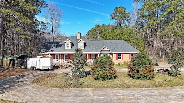 cape cod home with driveway, a porch, and a chimney