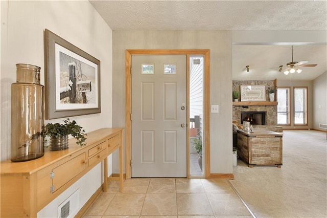 carpeted foyer with ceiling fan, a stone fireplace, and a textured ceiling