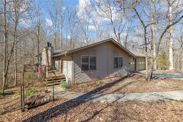 view of side of property featuring a garage, concrete driveway, crawl space, a wooden deck, and a chimney