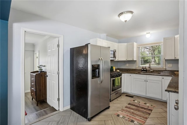 kitchen with white cabinets, appliances with stainless steel finishes, dark stone countertops, and sink