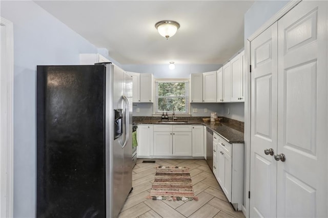 kitchen featuring stainless steel appliances, white cabinetry, sink, and dark stone counters