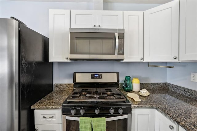 kitchen with stainless steel appliances, white cabinetry, and dark stone countertops