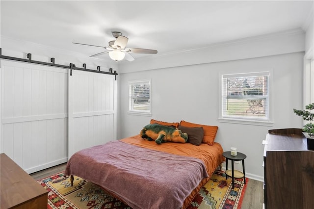 bedroom with ceiling fan, a barn door, crown molding, and hardwood / wood-style floors