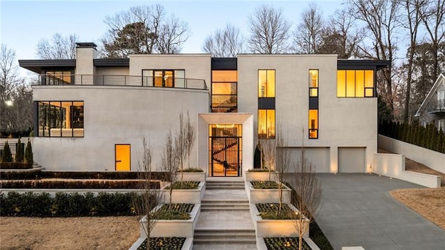 contemporary home with a balcony, driveway, a chimney, stucco siding, and a garage