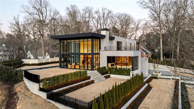 back of property featuring stucco siding, a balcony, a chimney, and fence