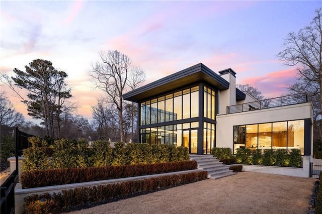 back of house at dusk featuring a balcony and a chimney