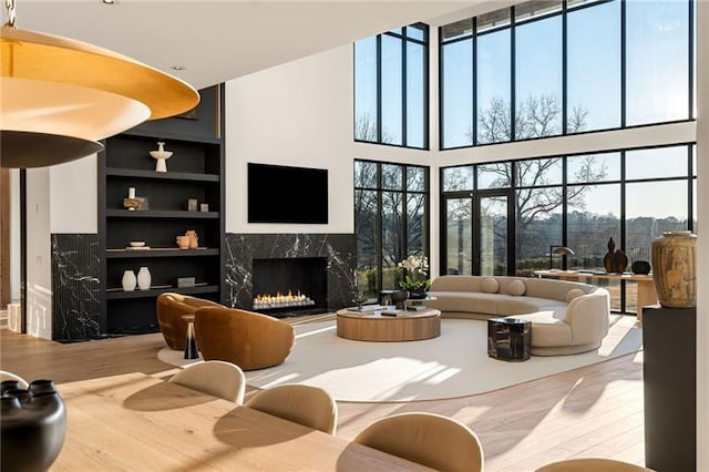 living room featuring a premium fireplace, built in shelves, wood finished floors, and a towering ceiling