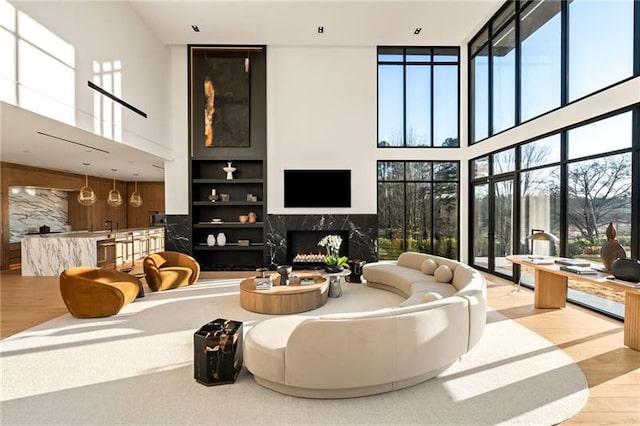 living room with a premium fireplace, built in features, a high ceiling, and wood finished floors