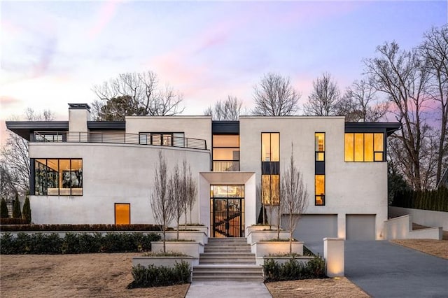 contemporary house with stucco siding, a garage, driveway, and a chimney