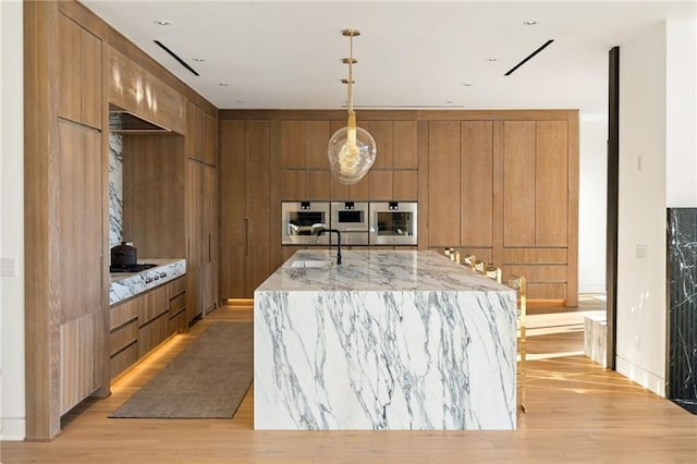 kitchen featuring light wood finished floors, light stone countertops, brown cabinetry, modern cabinets, and a sink