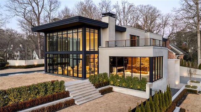 rear view of house featuring a balcony, fence, a sunroom, a chimney, and stucco siding