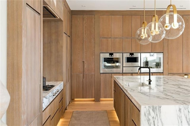 kitchen with light stone counters, brown cabinetry, an inviting chandelier, a sink, and modern cabinets