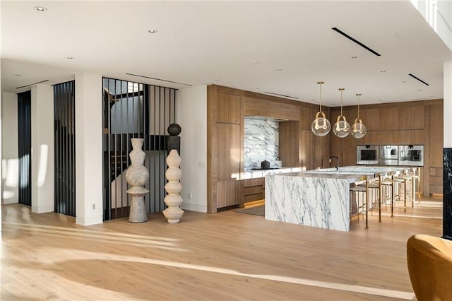 kitchen with a large island, modern cabinets, light wood-style flooring, brown cabinetry, and light countertops