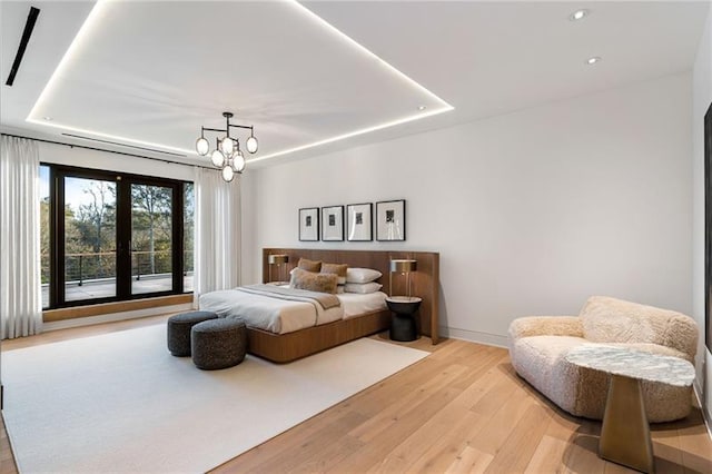 bedroom featuring an inviting chandelier, a raised ceiling, baseboards, and light wood finished floors