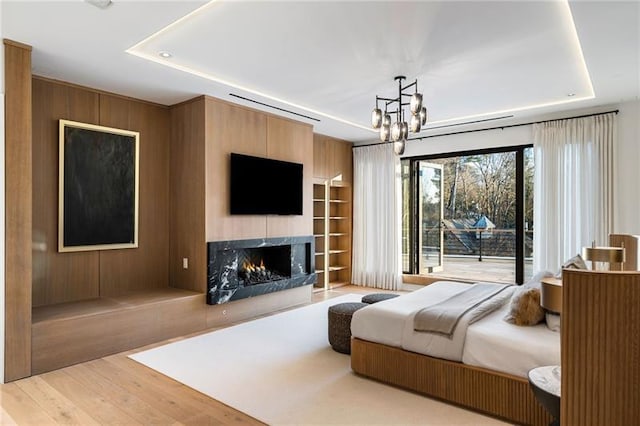 bedroom with a notable chandelier, a fireplace, a raised ceiling, and wood finished floors