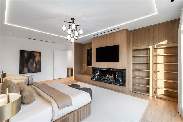 bedroom with a chandelier, recessed lighting, a fireplace, light wood-style floors, and a raised ceiling