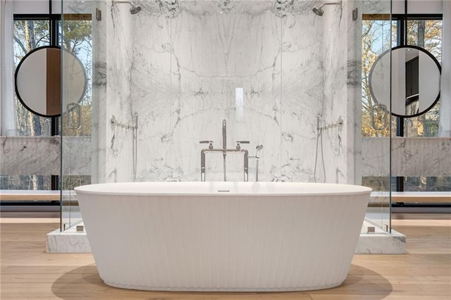 full bath with plenty of natural light, a freestanding bath, and wood finished floors