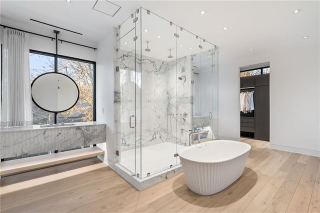 bathroom with a walk in closet, hardwood / wood-style flooring, a marble finish shower, a freestanding bath, and vanity