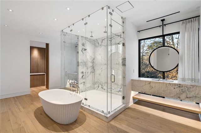 full bath with a freestanding tub, a marble finish shower, wood-type flooring, and recessed lighting