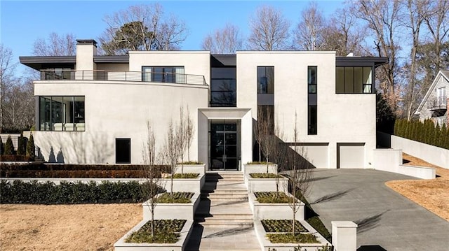 modern home with stucco siding, a chimney, a garage, a balcony, and driveway