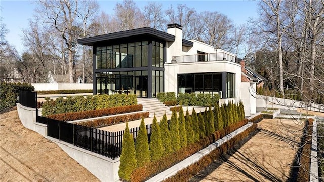 rear view of property with a balcony, fence, a chimney, and stucco siding