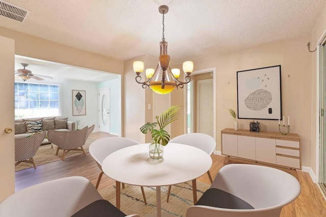 dining room with a textured ceiling, a notable chandelier, visible vents, baseboards, and light wood-style floors