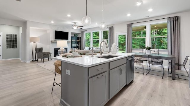 kitchen featuring ceiling fan, pendant lighting, stainless steel dishwasher, a center island with sink, and sink