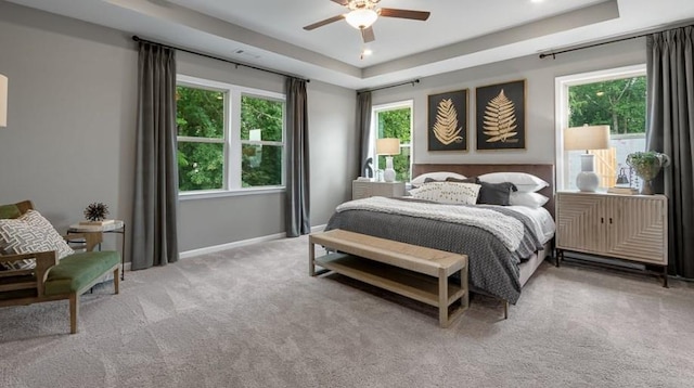 bedroom featuring ceiling fan, light colored carpet, and a tray ceiling