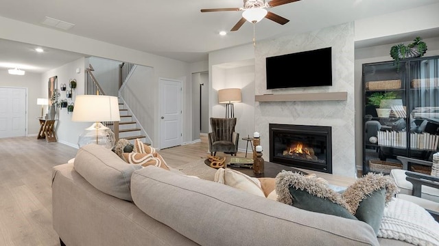 living room with light wood-type flooring, ceiling fan, and a high end fireplace