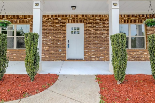 view of exterior entry with a porch and brick siding