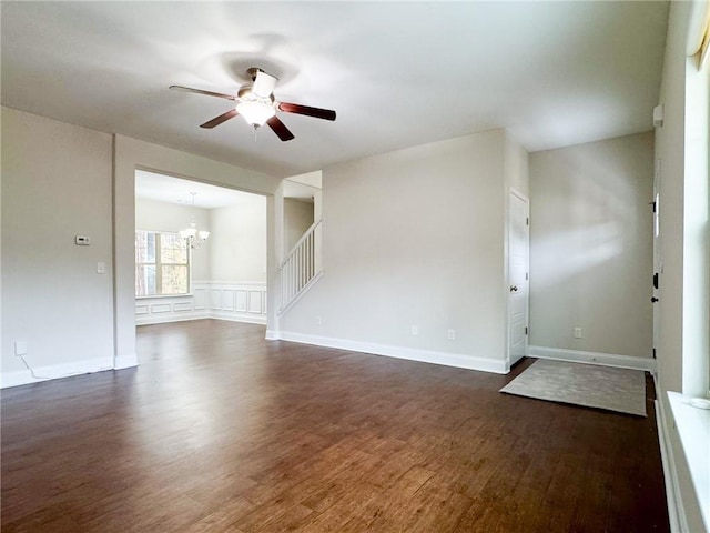 unfurnished living room featuring ceiling fan with notable chandelier, dark wood-style floors, and baseboards