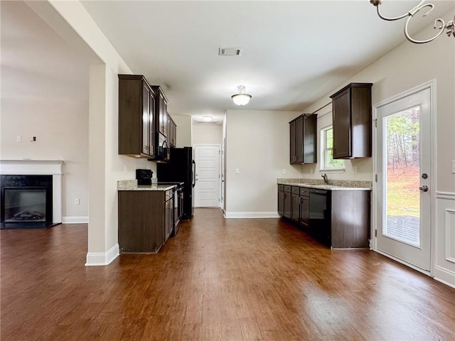 kitchen featuring visible vents, dark wood finished floors, black appliances, dark brown cabinets, and a glass covered fireplace