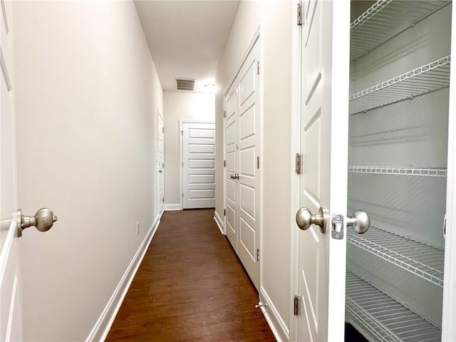 corridor with visible vents, baseboards, and dark wood-style flooring