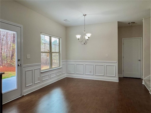 unfurnished dining area with dark wood finished floors, a wainscoted wall, visible vents, and an inviting chandelier