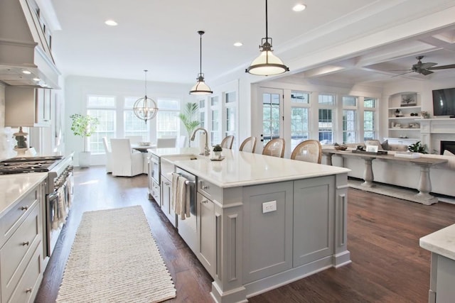 kitchen featuring a center island with sink, stainless steel appliances, dark wood-type flooring, decorative light fixtures, and ceiling fan with notable chandelier