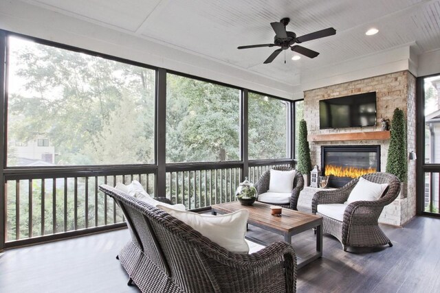 sunroom featuring a stone fireplace and ceiling fan