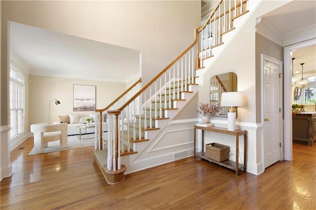 staircase featuring a decorative wall, crown molding, visible vents, and wood finished floors