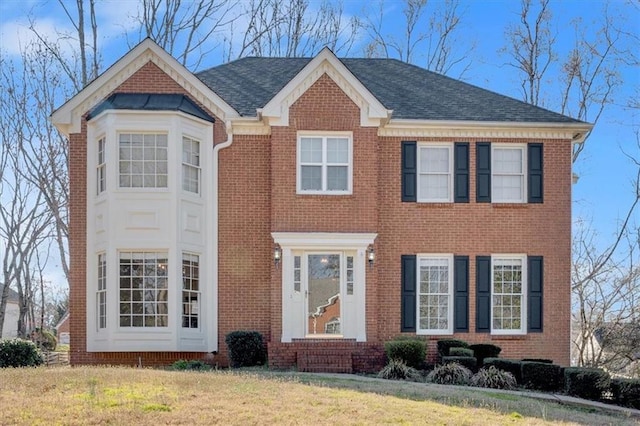 view of front of house with brick siding, a front yard, and a shingled roof